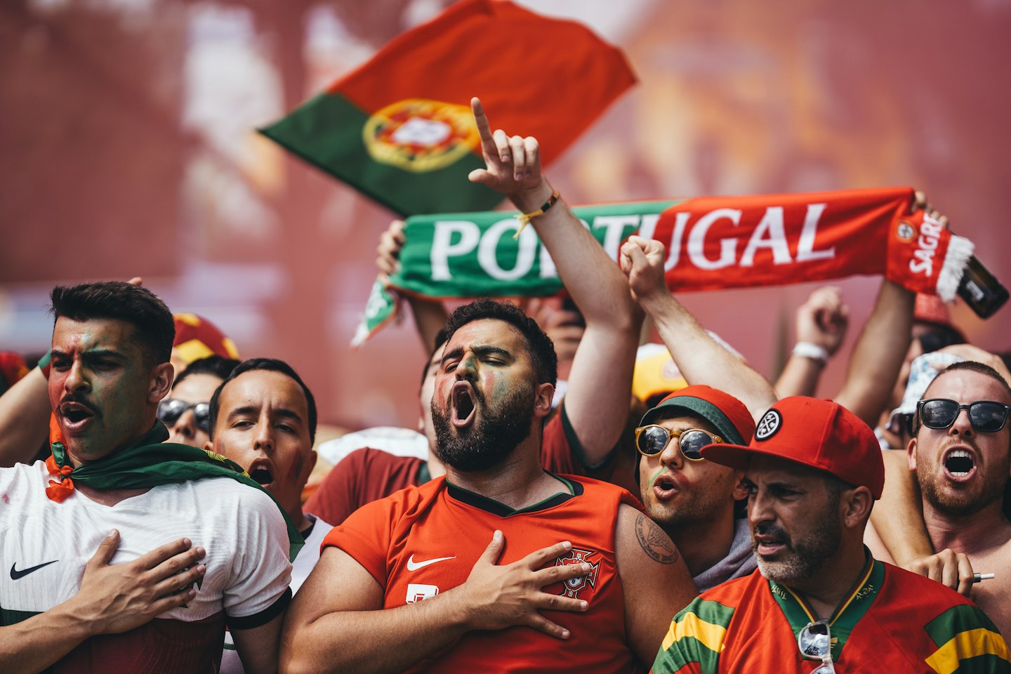 Soccer fans wearing red and green jerseys cheer with painted faces.